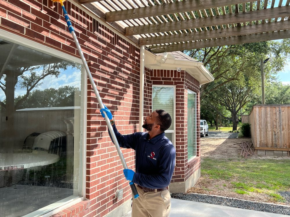 A Life After Bugs technician using a long pole brush to clear webs from the wooden eaves of a brick home