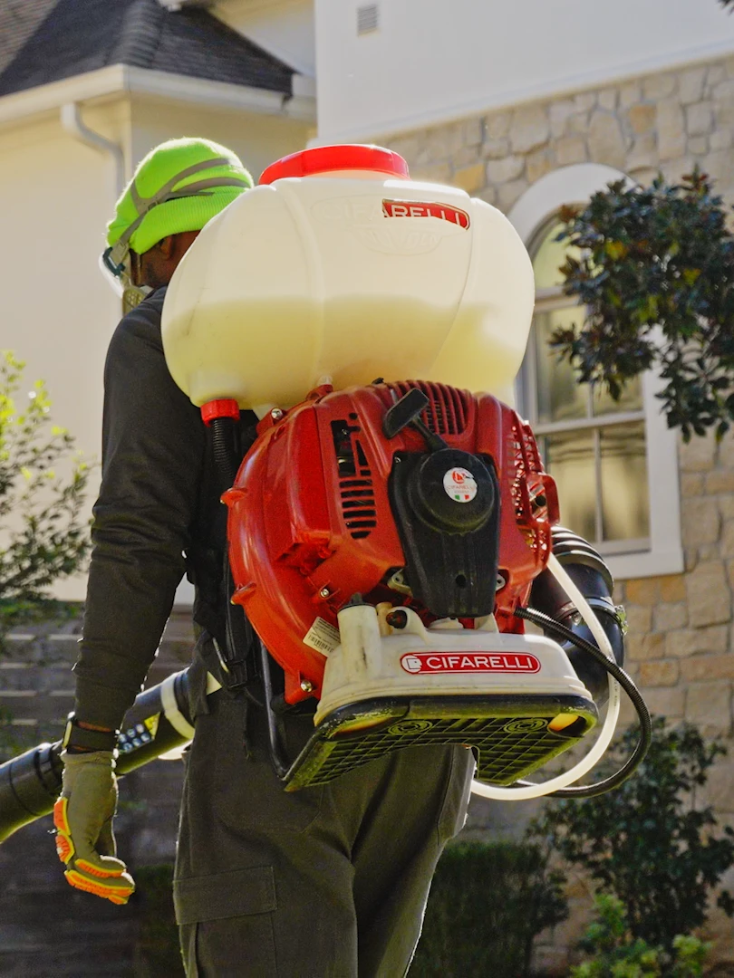 A technician treating the exterior of a suburban home with a backpack mist blower